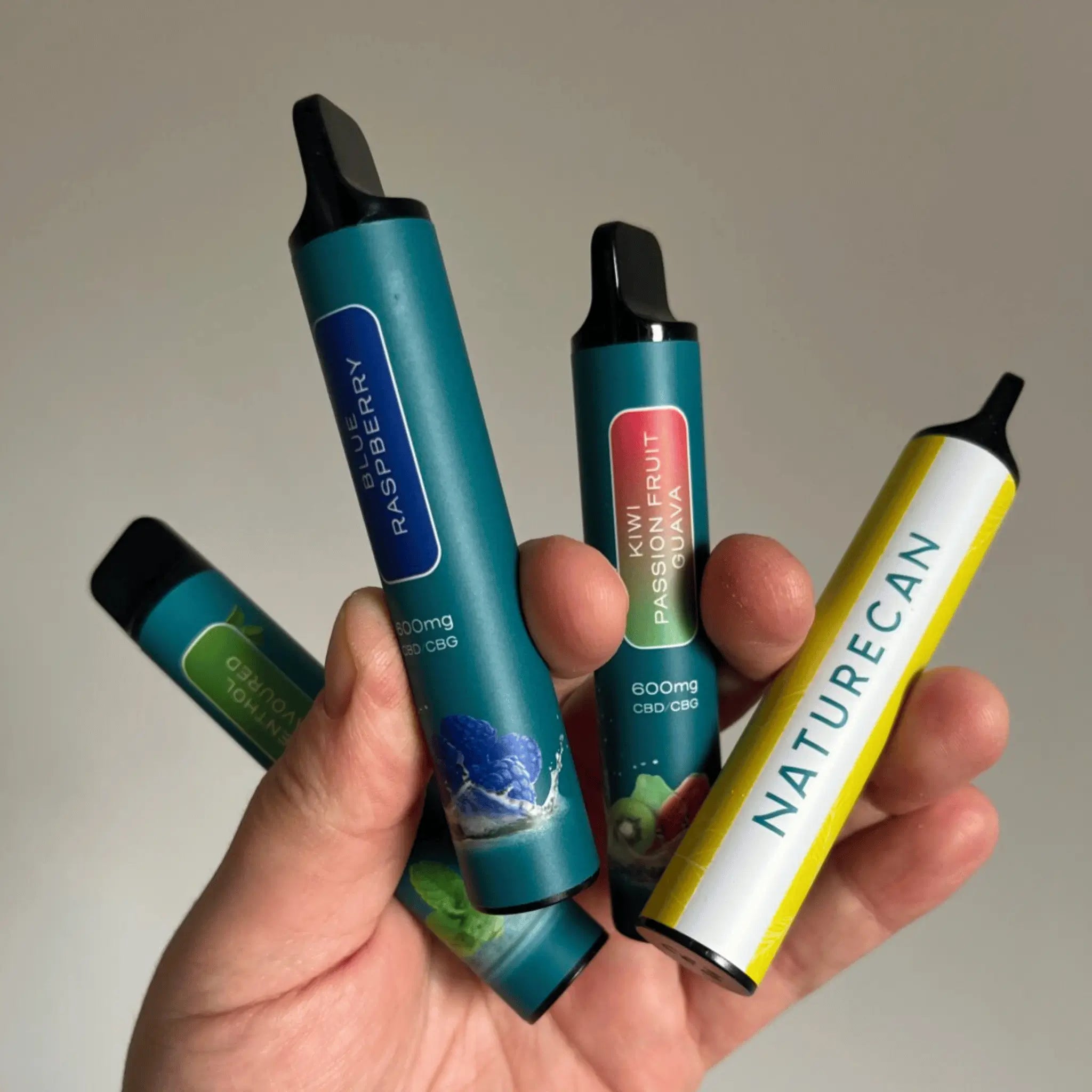 Hand holding multiple CBD/CBG Disposable Vape Devices with visible flavors like