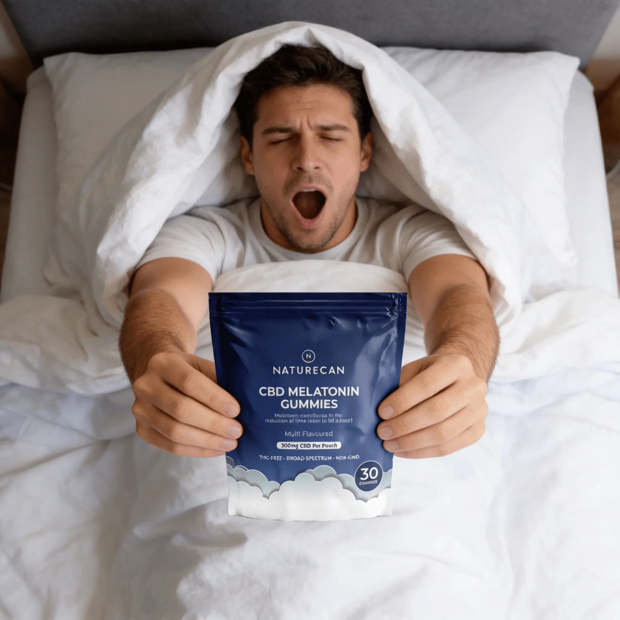 Man in bed holding a package of Naturecan CBD Melatonin Gummies
