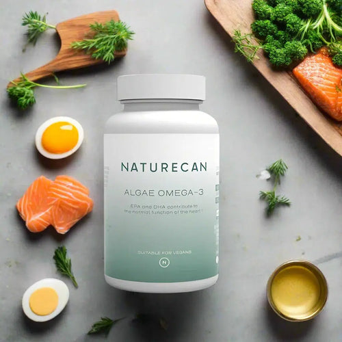 A bottle of "Naturecan Algae Omega-3" is placed among salmon, eggs, and greens on a kitchen counter.