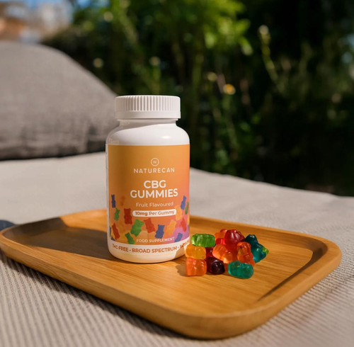 A jar of CBG Gummies with a colorful label sits on a wooden tray next to assorted gummy bears.