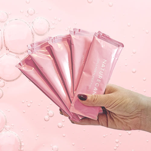 Hand holding pink Collagen Sachets against a bubble-filled pink background.