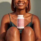 A smiling woman in a teal satin camisole sits with her knees drawn up, holding a white bottle of NatureCan Myo-Inositol supplements. The background is a clean, neutral gray wall with warm sunlight casting soft shadows.
