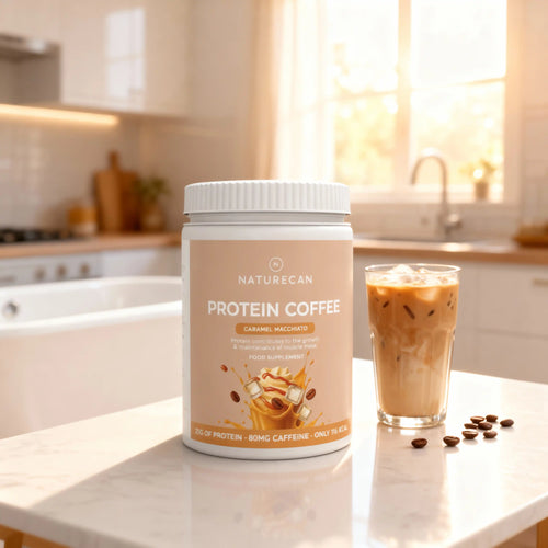 Protein Coffee jar labeled "Caramel Macchiato" on a kitchen counter with an iced coffee and coffee beans.