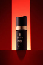 Skincare serum bottle with gold and black design on a red background